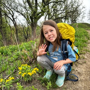 6 year old girl is waving next to flowers that match her pack