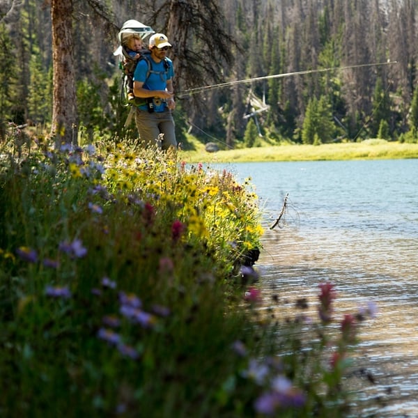A happy parent fishing with his son in the Deuter Kid Carrier.