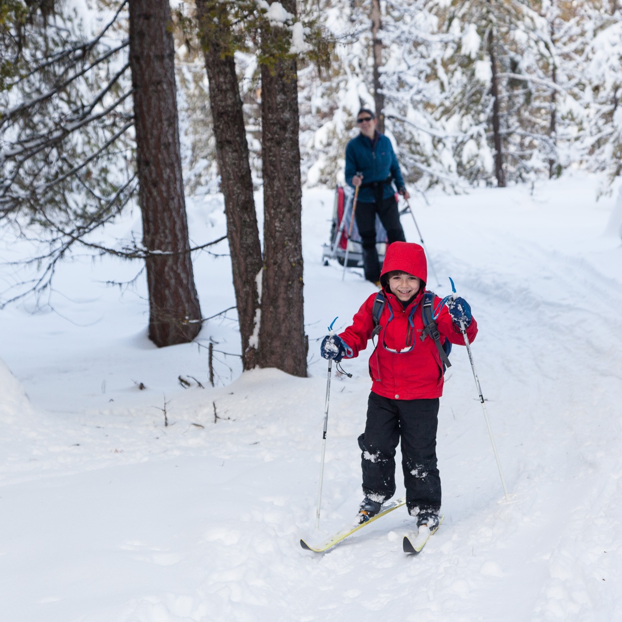 Smiling kid and mother cross-country skiing. 