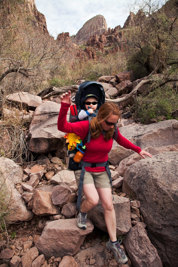Female hiker carrying infant in backpack carrier descends a rocky section of the Siphon Draw trail in the Superstition Mountains east of Phoenix, Arizona.